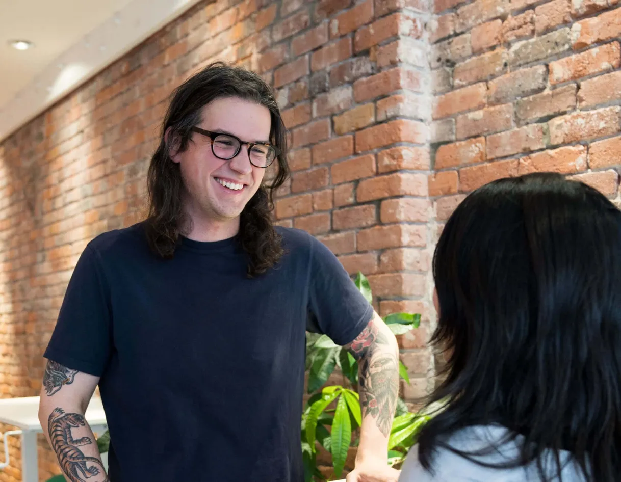 A photo highlighting foto.umbii.boo's small but impactful team, with a smiling team member with tattoos and glasses chatting in the office