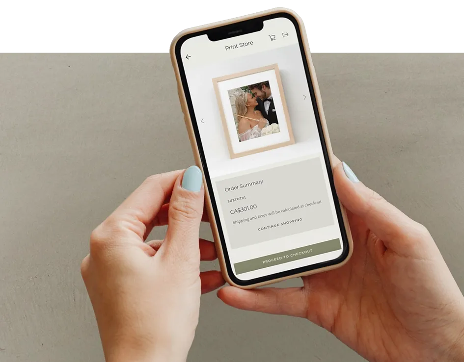Hands holding a smartphone displaying foto.umbii.boo Print Store checkout screen with a framed wedding photo.